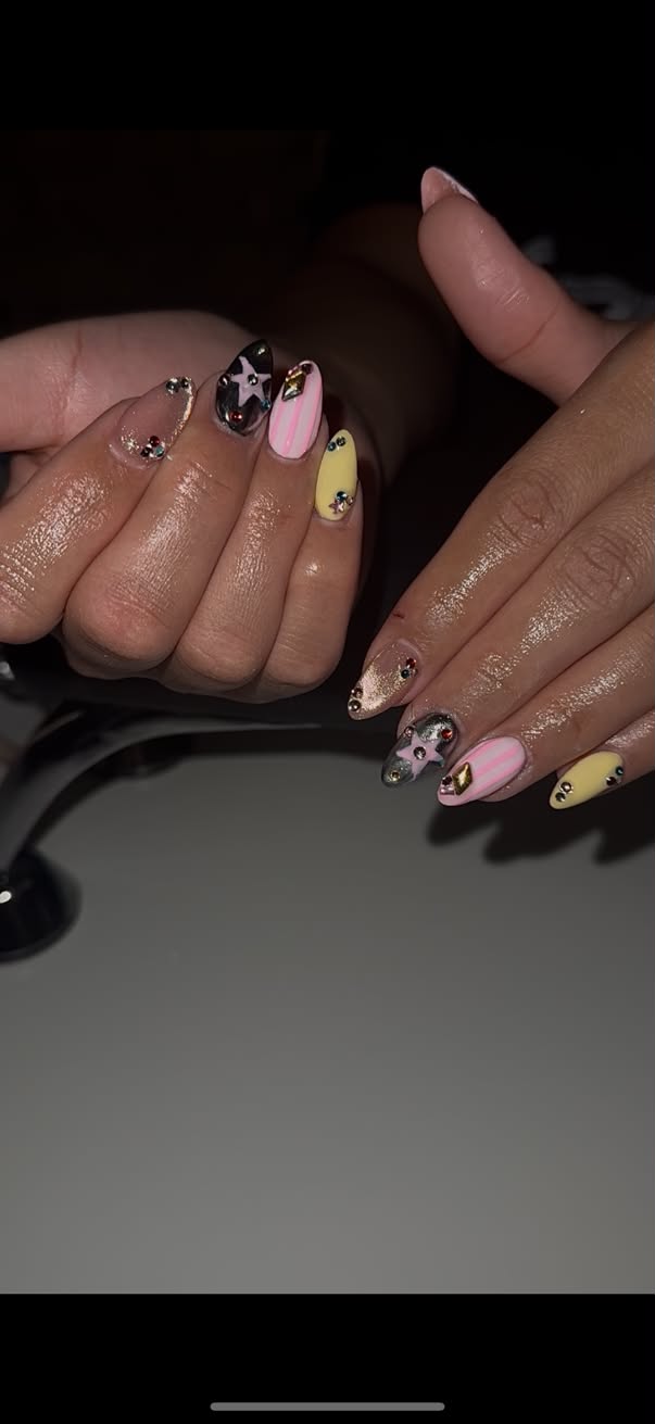 Almond nails in pink stripes, yellow and black chrome stars with gold charms